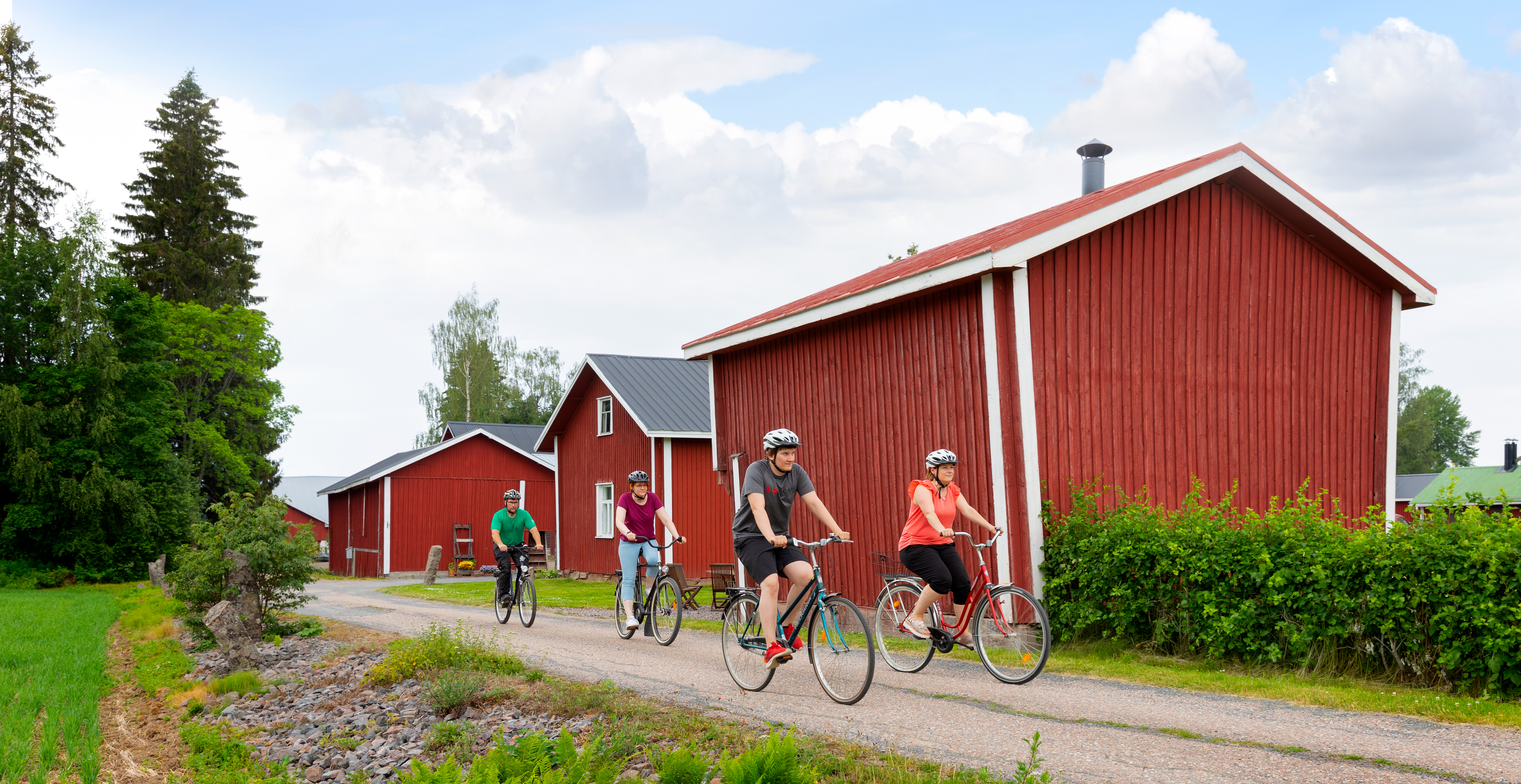 Pyöräilijöitä ja vanhoja raknnuksia Ruokojärven kulttuurimaisemassa aurinkoisena kesäpäivänä