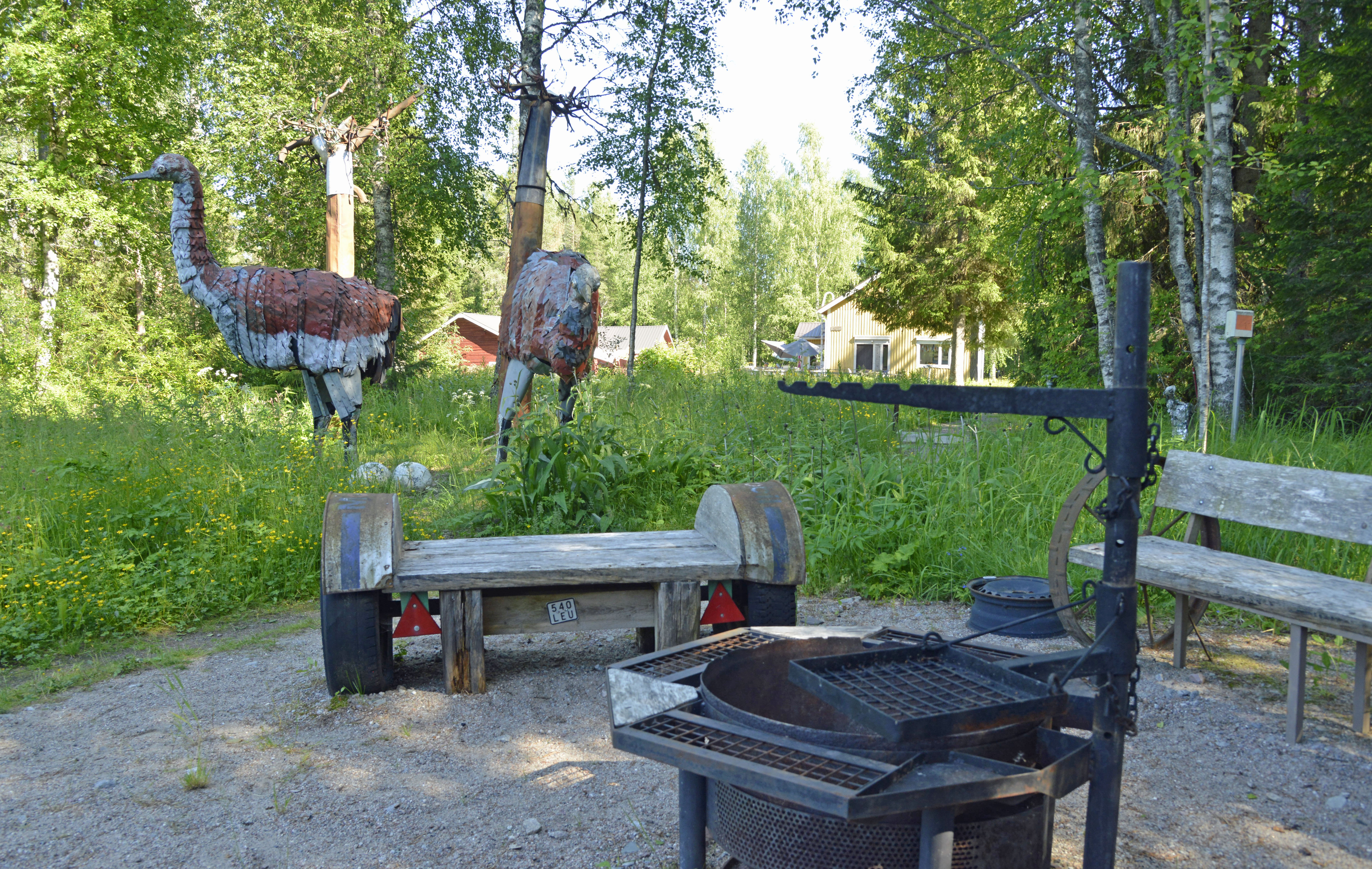 Nuotiopaikka Alpon Savannilla, keltainen talo ja puita taustalla